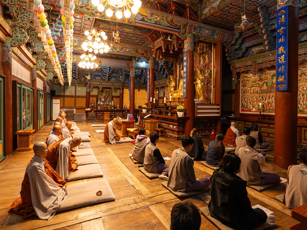 Les moines du temple Baekyangsa et un groupe de journalistes venus y passer la nuit participent à la prière du matin, le 3 mai 2025. Le sanctuaire principal, en bois, est décoré selon le style coloré du dancheong. © Ministère de la Culture, des Sports et du Tourisme