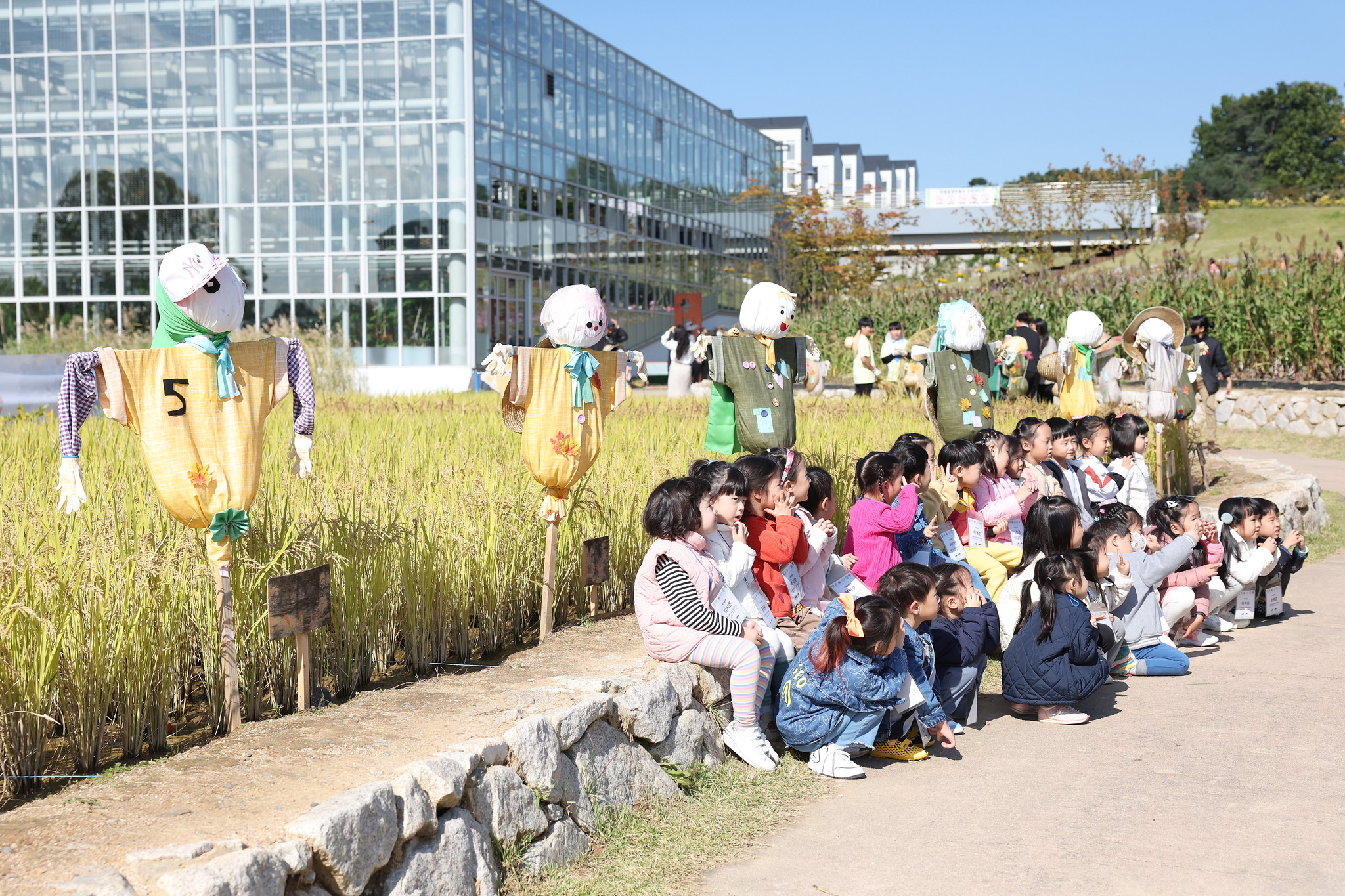 Un groupe de jeunes enfants pose aux côtés d’épouvantails dressés dans une rizière du Musée national de l’agriculture, à Suwon, le 22 octobre 2025. © Lee Jeong Woo / Korea.net