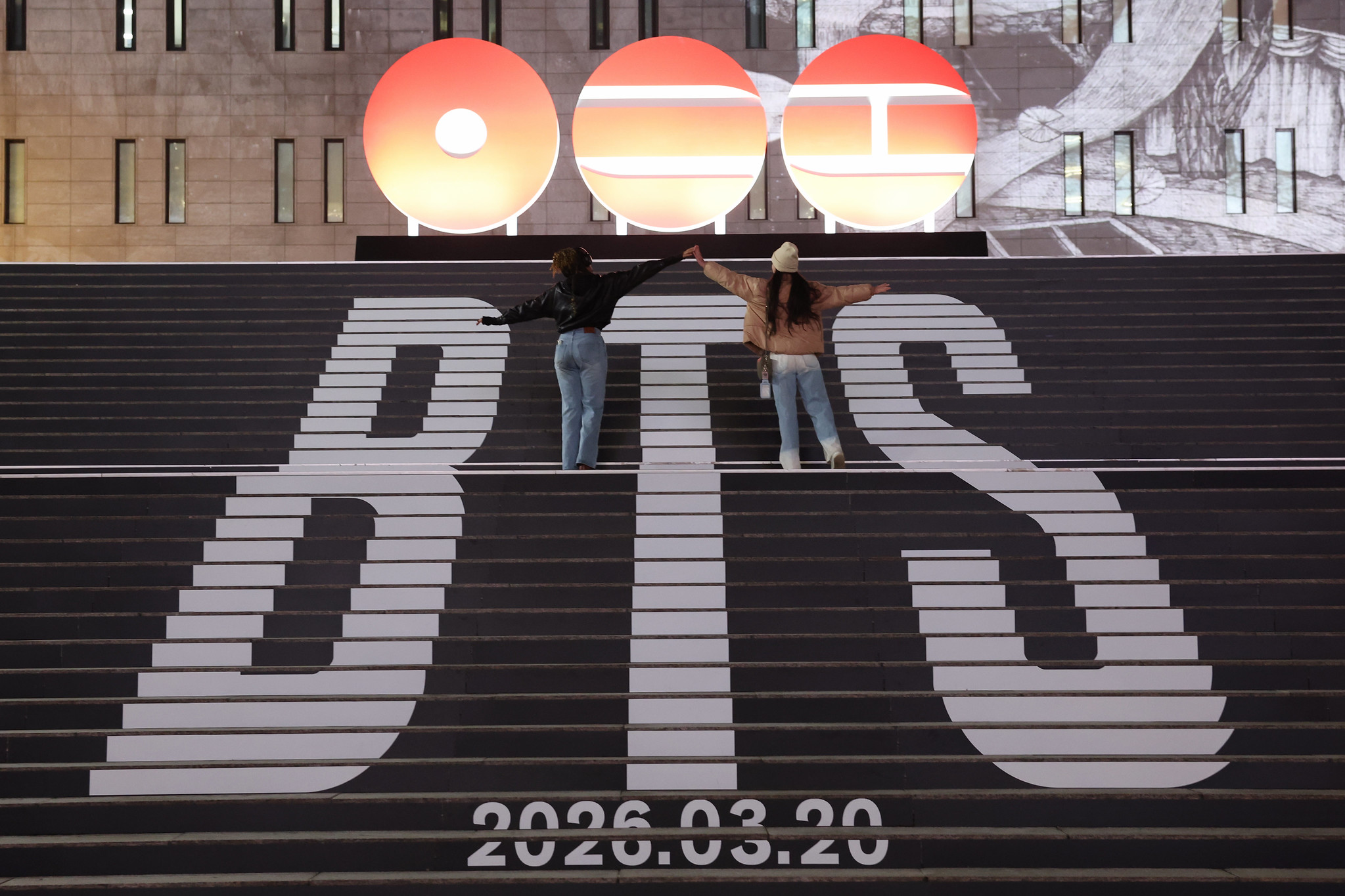Deux personnes dansent sur le grand escalier du Sejong Center for the Performing Arts, à Séoul, décoré du logo du groupe BTS, le 6 janvier 2026. © Cheong Wa Dae
