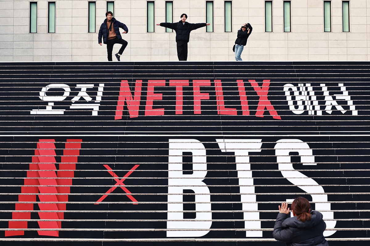 Trois personnes posent au sommet des escaliers du Sejong Center for Performing Arts, décorés à l’effigie du prochain concert de BTS marquant leur grand retour, le 11 mars 2026. © Agence de presse Yonhap 