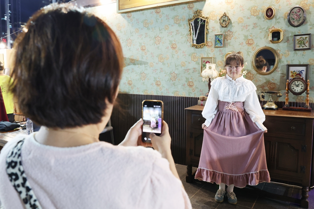 Une jeune femme vêtue d’un costume des années 1950 se fait prendre en photo dans un espace reconstitué évoquant le quotidien de cette décennie et installé dans le cadre de Busan Heritage Night, le 25 juillet 2026. © Park Dae-jin / Korea.net