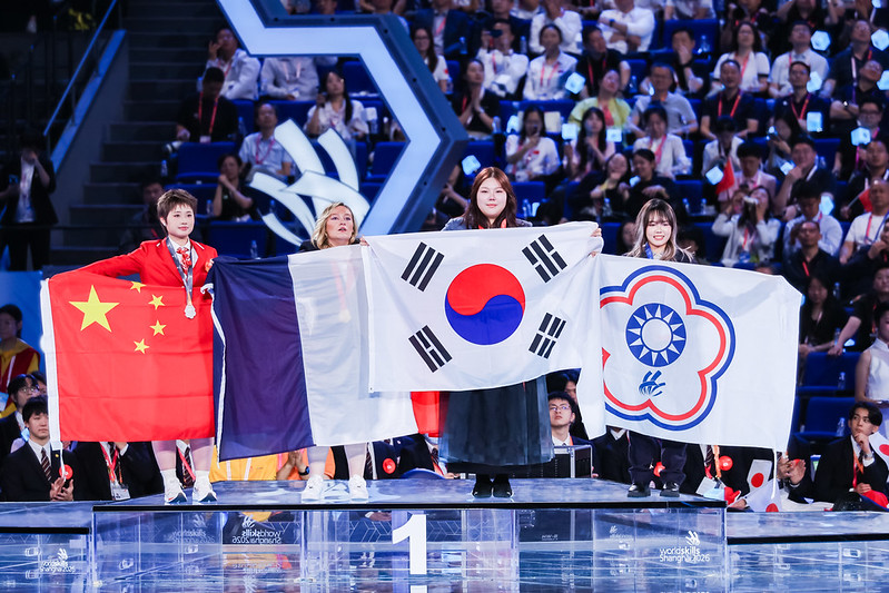 Kim Jo-young, médaillée d’or en coiffure, porte le drapeau coréen lors de la cérémonie de clôture du WorldSkills 2026 au National Exhibition and Convention Center à Shanghai, le 27 septembre 2026. © WorldSkills