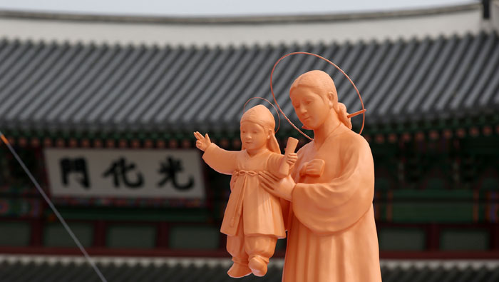 프란치스코 교황이 집전하는 시복식 미사 제단 앞에 한복을 입은 성모 마리아 상과 아기예수 상이 광화문을 배경으로 서 있다. 