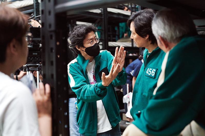 Korea.net a nommé Hwang Dong-hyuk (au centre), réalisateur de la série originale Netflix « Squid Game », la personnalités de l'année 2021. Le réalisateur Hwang discute avec l'acteur Lee Jung-jae (deuxième à partir de la droite) sur le plateau. © Netflix