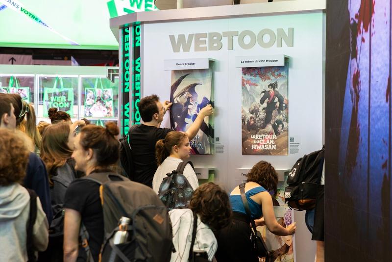 Des participants décrochent des posters au pavillon de Naver Webtoon dans la zone spéciale Amazing de la Japan Expo de Paris, en juillet 2023. © Naver Webtoon