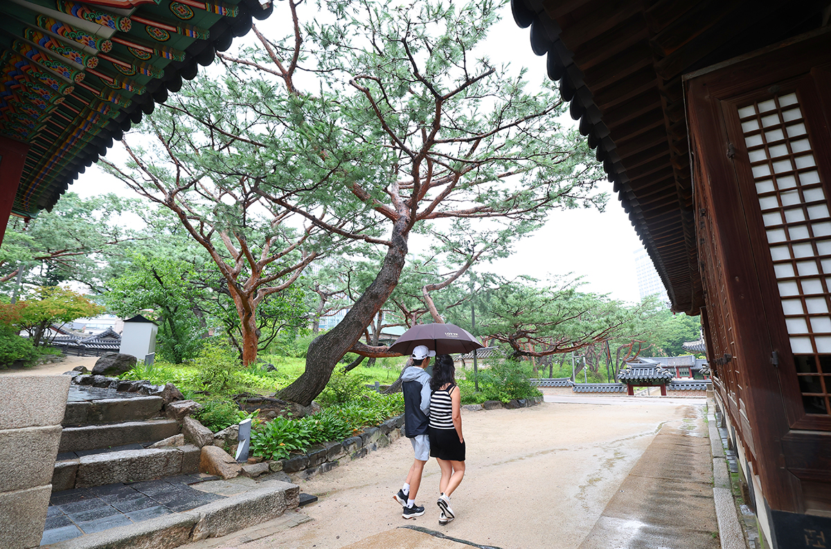 Deux personnes s’abritant sous un parapluie font une promenade dans le palais Deoksugung, à Séoul, le 16 juillet 2025. © Lee Jeong Woo / Korea.net