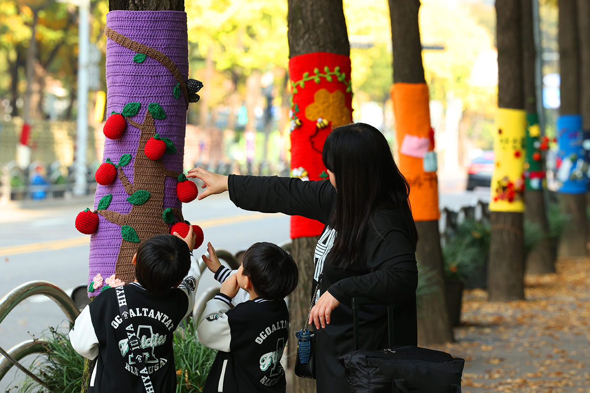 Une famille passe devant les arbres encharpés d’une rue de Gwangmyeong, dans le Gyeonggi, le 7 novembre 2025. 