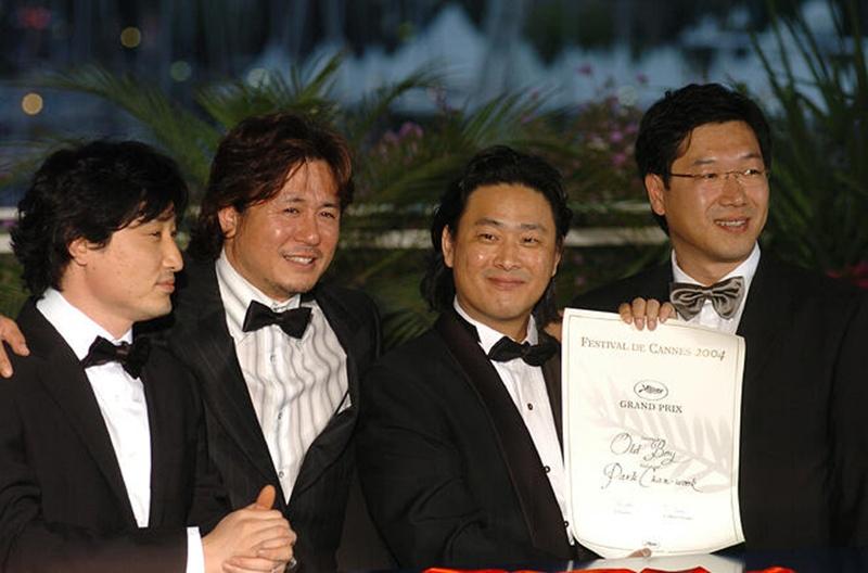 De gauche à droite : le producteur Lim Seung-yong, l'acteur Choi Min-sik, le réalisateur Park Chan-wook et le directeur de la photographie Chung Chung-hoon posent pour célébrer la victoire du film Oldboy, élu Grand Prix du 57e Festival de Cannes, le 22 mai 2004. © Médiathèque officielle du Festival de Cannes
